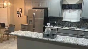 Cozinha com bancadas de granito, eletrodomésticos de aço inoxidável e área de bar com banquetas.