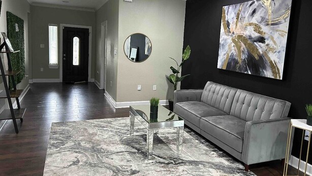 Uma sala de estar moderna com um sofá cinzento, uma mesa de centro de vidro e uma grande pintura abstrata na parede.