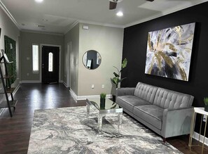 A modern living room with a grey sofa, a glass coffee table, and a large abstract painting on the wall.