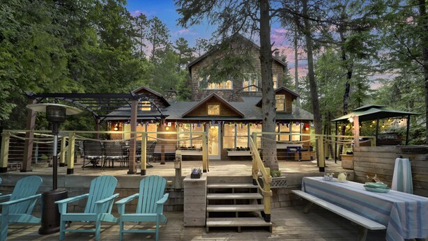 A wooden deck with Adirondack chairs, a picnic table, and a staircase leading to a lodge.