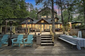 Une terrasse en bois avec des fauteuils Adirondack, une table de pique-nique et un escalier menant à un chalet.