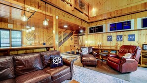 A cozy cabin interior with a wooden interior, leather furniture, a staircase, and nautical-themed decor.