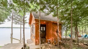 A wooden cabin with a dock, surrounded by trees and overlooking a body of water.