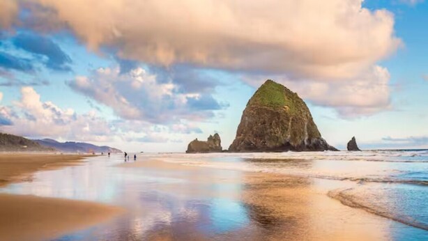 A beach with a prominent rock formation and calm waters.