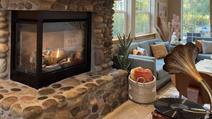A stone fireplace with a built-in TV, a wooden shelf with decorative items, and a cozy seating area with a sofa and a vintage record player.