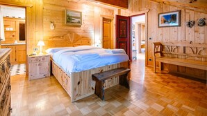 Un dormitorio de cabaña de madera con cama, mesita de noche, banco y paredes de madera.