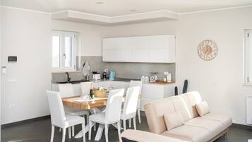Una cucina moderna con mobili bianchi, un tavolo da pranzo con sedie e un divano beige in un soggiorno luminoso.