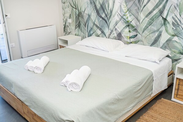 A neatly made bed with white linens and rolled towels, a white bedside table, and a wall with a leafy pattern. - Marilù Dream House Formia, Villa 800 meters from the sea (Formia)