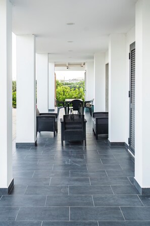 A covered outdoor area with dark tiled flooring, white walls, and black wicker furniture.