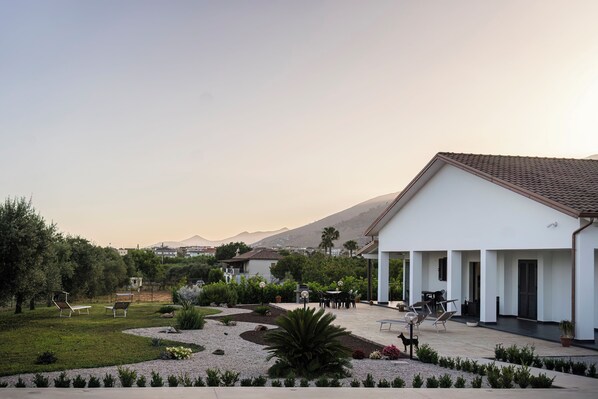 A courtyard with outdoor seating, a white building with a tiled roof, and landscaped gardens.