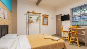 A bedroom with a bed, a desk, and a chair. There is a TV on the wall and a window with blinds. - Studio Apt. 316/fee Cleaning Free! (Medellín)