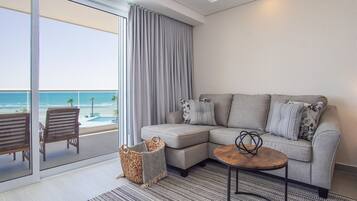 A modern living room with a grey sectional sofa, a small wooden coffee table, and a view of the beach through large sliding glass doors.