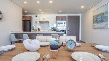 A modern kitchen with a central island, a dining area with a wooden table set for four, and a living area with a sofa and decorative items.