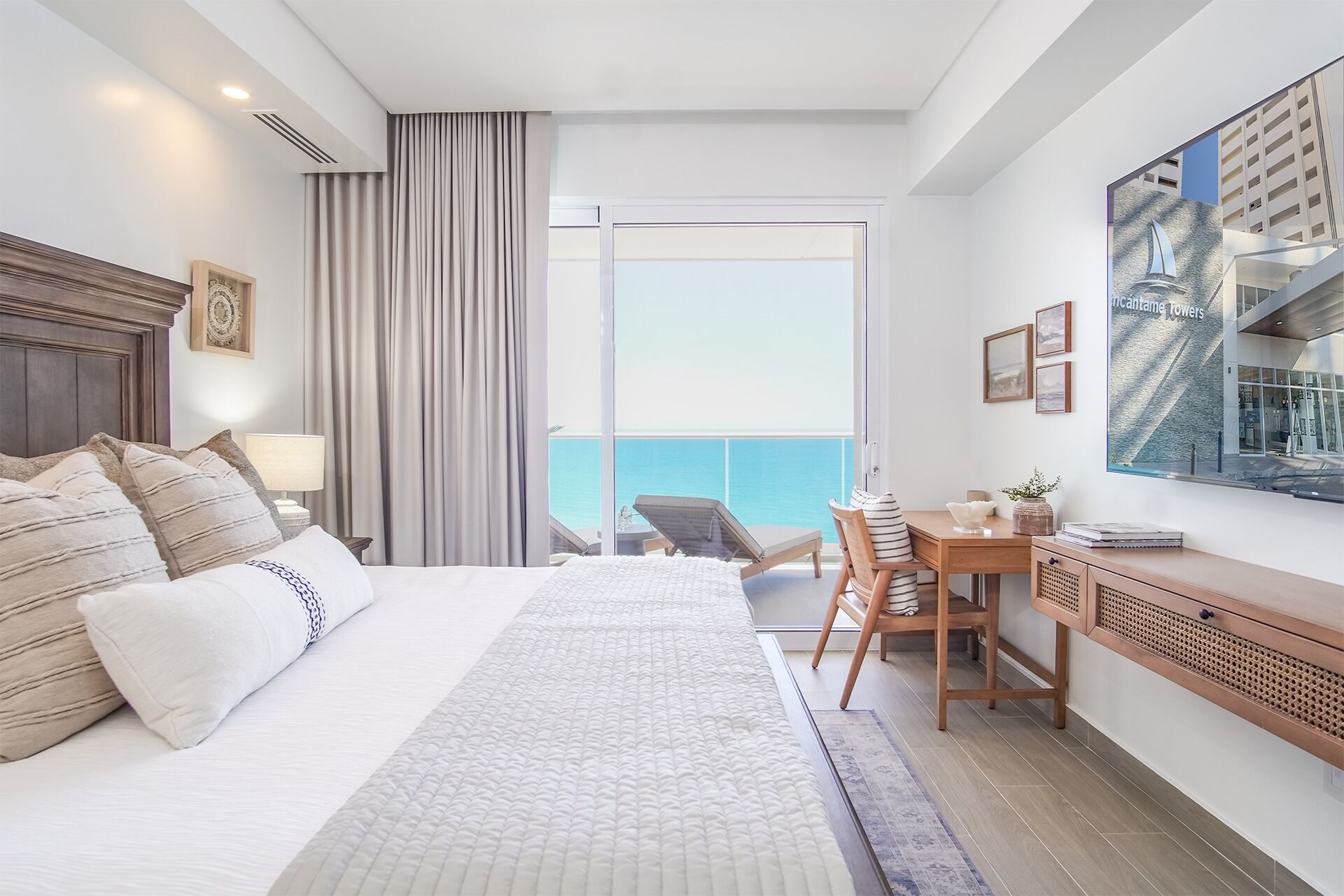Quarto de hotel com cama grande, escrivaninha, cadeira e vista para o oceano.