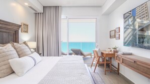 Habitación de hotel con una cama grande, un escritorio, una silla y vista al océano.