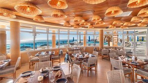 Un restaurante con mobiliario de mimbre, amplias ventanas y vista al océano.