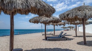 Una playa con sombrillas de paja, sillas de descanso y una vista despejada del océano.