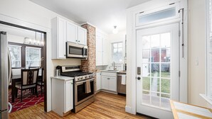 A modern kitchen with white cabinets, a brick accent wall, a stainless steel stove, and a large window. - Spacious 4BD 2BA Home Near OSU (Columbus)