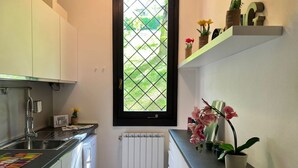 A compact kitchen with white cabinets, a black countertop, a window with a diamond pattern, and a potted orchid. - Bnbook Casa Luccio Vista lago-Ispra (ISPRA)
