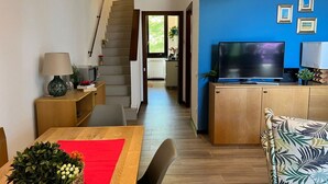 A modern living space with a staircase, a dining area with a red table runner, a television, and a kitchen area with wooden cabinets. - Bnbook Casa Luccio Vista lago-Ispra (ISPRA)