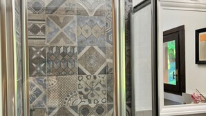 A bathroom with a variety of patterned tiles and a glass shower enclosure. - Bnbook Casa Luccio Vista lago-Ispra (ISPRA)