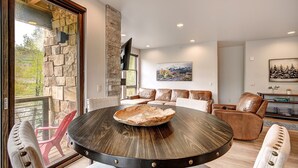 A modern living room with a stone accent wall, a round wooden table with a central bowl, leather sofas, and a mounted television. - Blue River Flats in Silverthorne, amazing location and panoramic mountain views (Silverthorne)