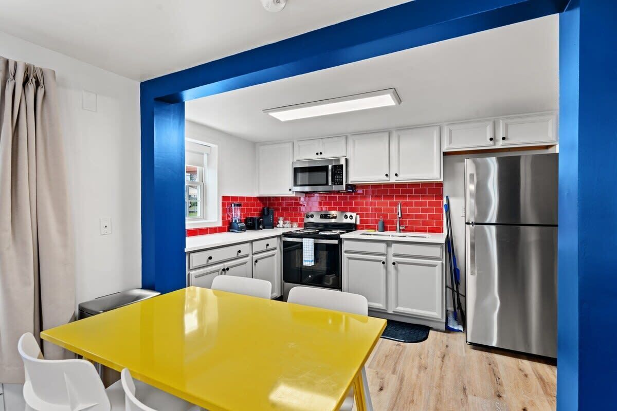A modern kitchen with white cabinets, red backsplash, stainless steel appliances, and a yellow table.