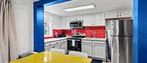 A modern kitchen with white cabinets, red backsplash, stainless steel appliances, and a yellow table.