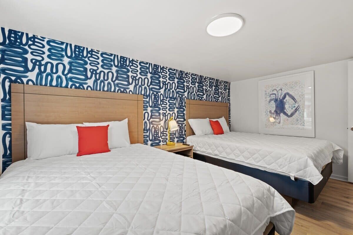A hotel room with two beds, a patterned wall, and a framed artwork.