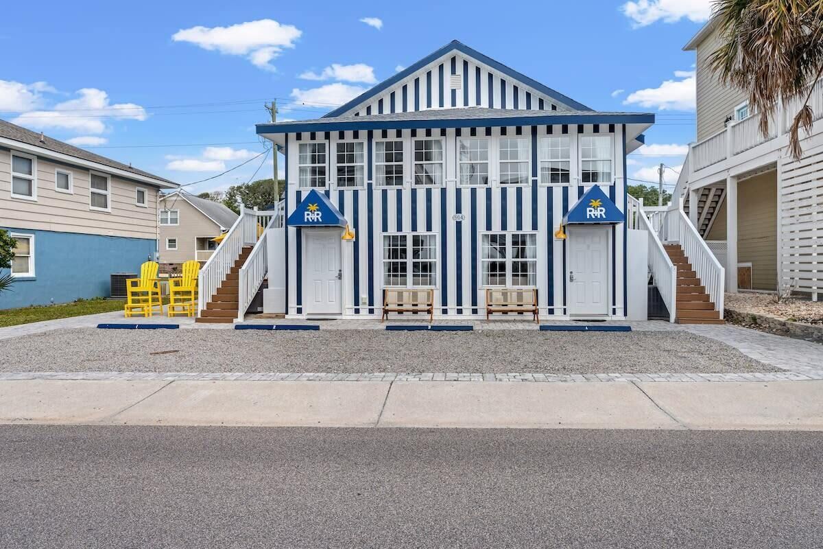 A two-story building with a blue and white striped facade, two doors marked with 'RVR' signs, and a small outdoor seating area with yellow chairs.