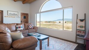 Un saló amb un sofà de cuir, una taula de centre, una finestra gran d'arc i vistes a un paisatge rural.
