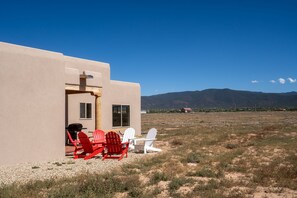 A building with a patio area featuring red and white Adirondack chairs, a grill, and a view of distant mountains.