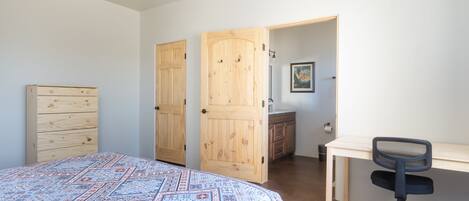 Un dormitorio con una cama, un aparador de madera, un escritorio con una silla y una puerta que da a otra habitación.