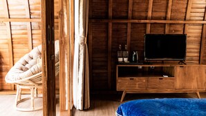 A wooden room with a television on a wooden cabinet, a wicker chair, and a bed with a blue blanket.