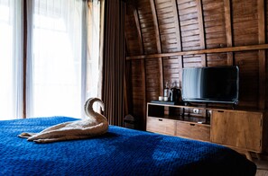 A hotel room with a bed, a wooden TV stand, a swan-shaped pillow, and a window with curtains. - Kabinku Bali (Baturiti)