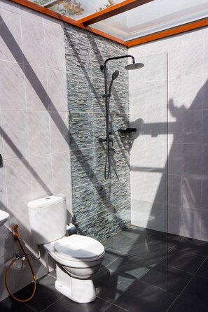 Un baño moderno con una pared de acento de piedra, cabina de ducha de vidrio y un inodoro blanco.