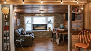 Un interior acogedor con pared de piedra, techo de madera, sofá de cuero, chimenea y zona de comedor con taburetes.