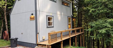 A two-story cabin with a wooden deck, surrounded by trees.