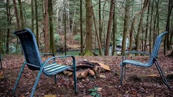 Two metal chairs in a forest setting with a fallen log and a stream in the background.