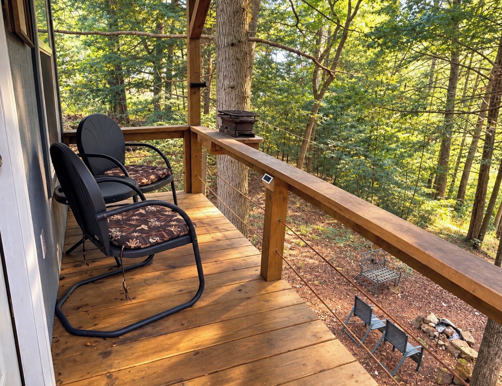 Une terrasse en bois avec deux chaises et une table, donnant sur une zone boisée.