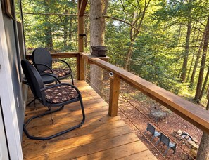 Eine Holzterrasse mit zwei Stühlen und einem Tisch, mit Blick auf ein bewaldetes Gebiet.