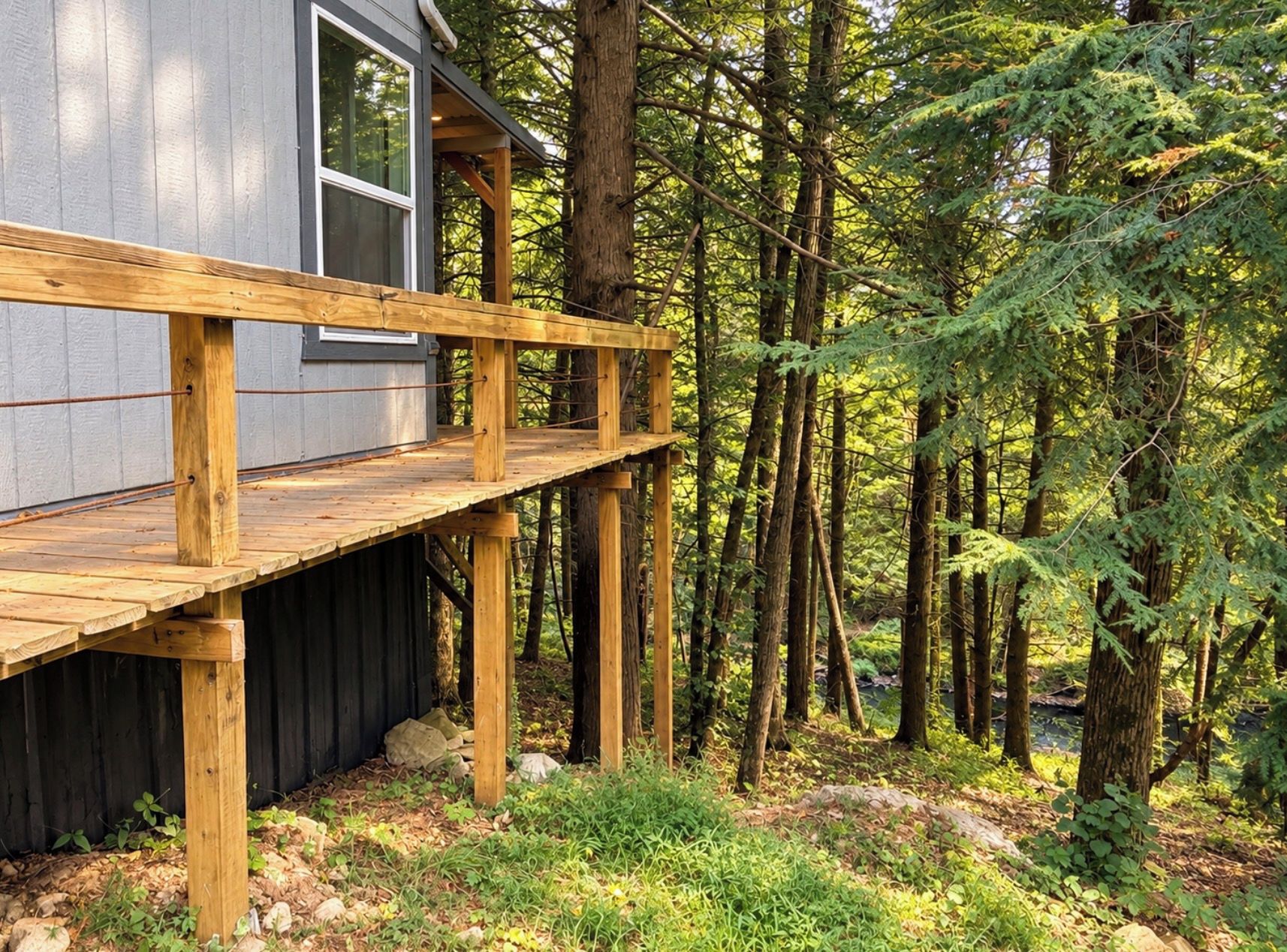 A cabin with a wooden deck, surrounded by dense forest.
