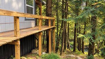 A cabin with a wooden deck, surrounded by dense forest.