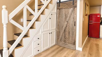 A staircase with white railings and wooden steps, leading to a room with a wooden door and a red appliance.