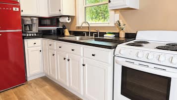 Une cuisine moderne avec des meubles blancs, un réfrigérateur rouge, une cuisinière et une machine à café.