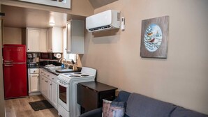 A compact kitchen with a stove, refrigerator, and microwave. There's a couch and a painting on the wall.