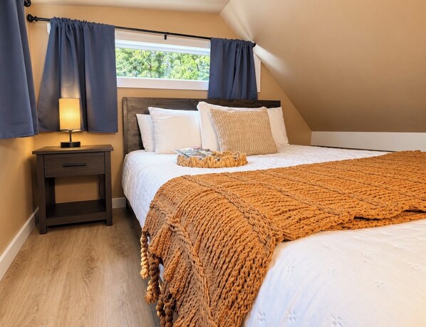 A bedroom with a bed, a bedside table with a lamp, and a window with curtains.