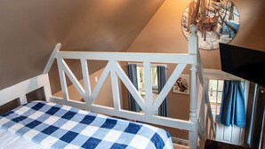 A bedroom with a checkered bedspread, a white headboard, a ceiling fan, and a wall-mounted painting of deer.
