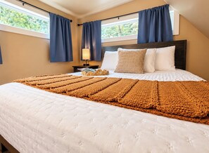 A bedroom with a large bed, a nightstand, a lamp, and a window with curtains. - Hemlock Cabin at Ranger Creek - Near Coalmont OHV Park! (Coalmont)