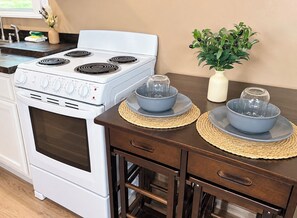 Una cucina con un piano cottura bianco, due ciotole blu su sottopiatti di rattan e un vaso con foglie verdi su un tavolo di legno.